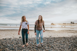 Two women walking on beach wearing nöz orange and blue sunscreen laughing